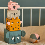 The Roommate Jungle Life Stacking Blocks placed on a bed next to a fabric ball. 