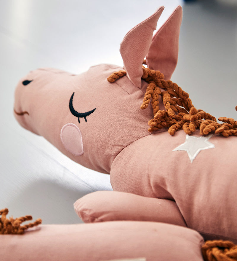 Close up of the Roommate childrens organic cotton lazy long horse cushion in the old rose colour on a grey background