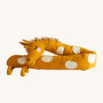 Roommate Long Organic Giraffe Cushion. A sleepy, smiling, long giraffe cushion in mustard yellow with cream spots, a curly mane and 4 small legs