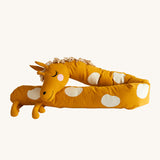 Roommate Long Organic Giraffe Cushion. A sleepy, smiling, long giraffe cushion in mustard yellow with cream spots, a curly mane and 4 small legs