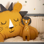 The The Roommate Lion Rag Doll toy propped up against a large Roommate cushion