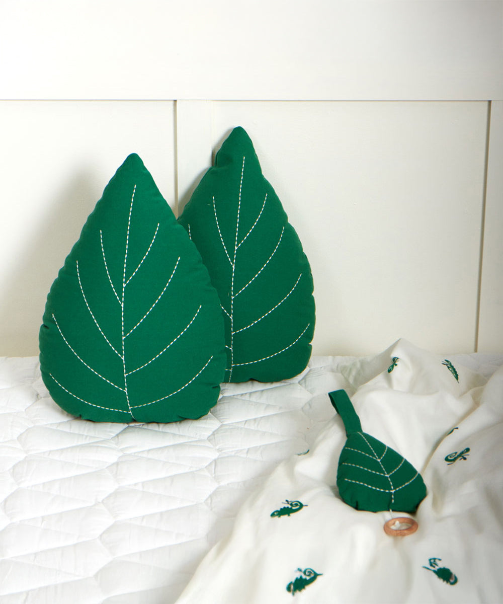 The Roommate Leaf Lullaby Music Mobile laying on a bed with two Roommate green Leaf cushions in the background