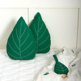The Roommate Leaf Lullaby Music Mobile laying on a bed with two Roommate green Leaf cushions in the background