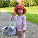A child wearing a pink Roommate Mouse bucket hat in a park.