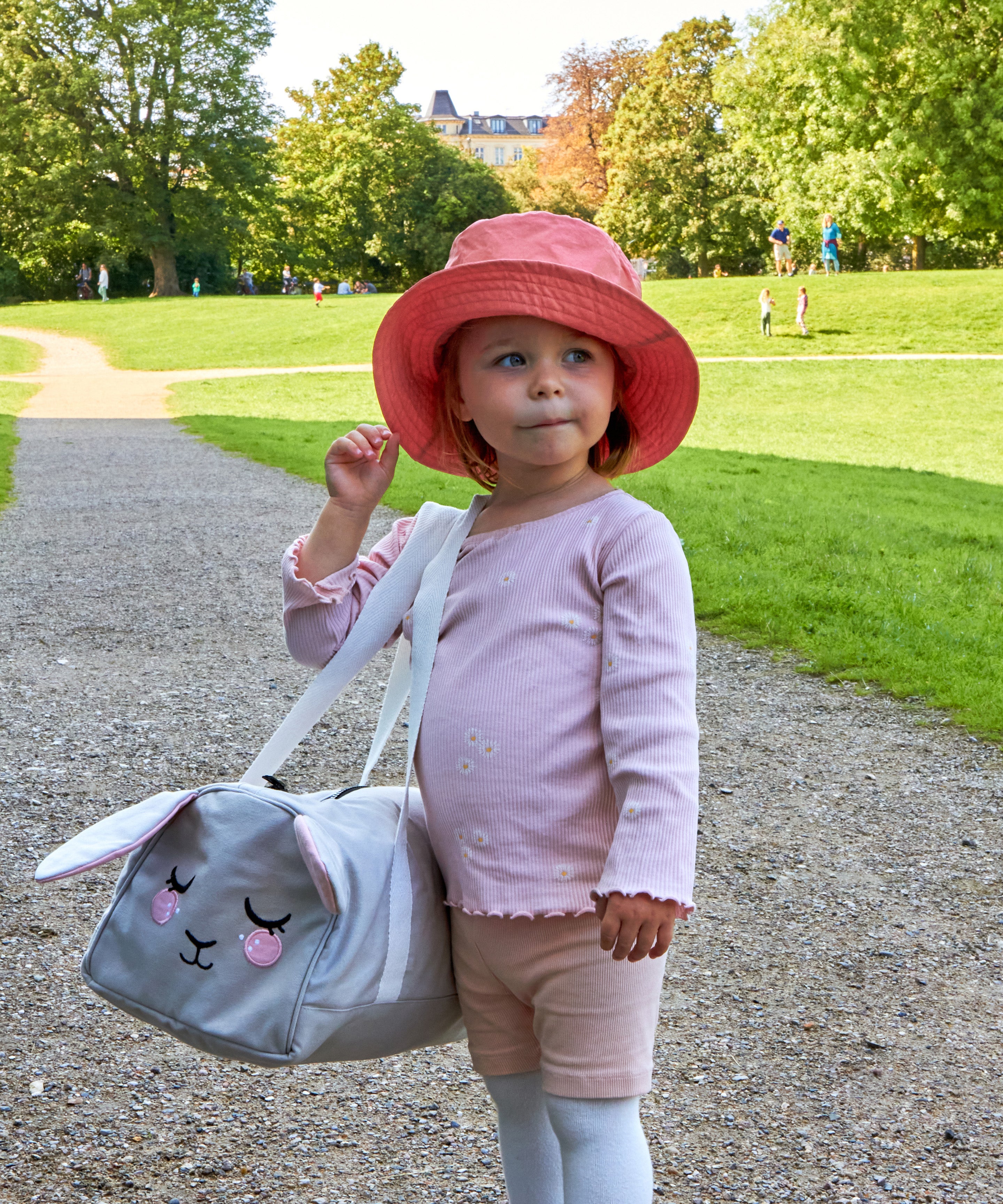 A child wearing a pink Roommate Mouse bucket hat in a park.