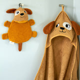 Roommate dog washcloth bath toy hanging on a wall hook next to a matching dog hooded towel, showing how the built-in loop is used for drying after bath time.