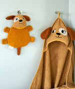 Roommate dog washcloth bath toy hanging on a wall hook next to a matching dog hooded towel, showing how the built-in loop is used for drying after bath time.