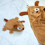 Roommate dog washcloth bath toy placed beside a matching dog hooded towel on a pale marble surface, showing coordinating organic cotton bathroom textiles.