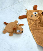 Roommate dog washcloth bath toy placed beside a matching dog hooded towel on a pale marble surface, showing coordinating organic cotton bathroom textiles.