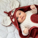 A little baby wrapped up in the Roommate organic cotton hooded towel, in red with a cute red panda face embroidered onto the hood. 
