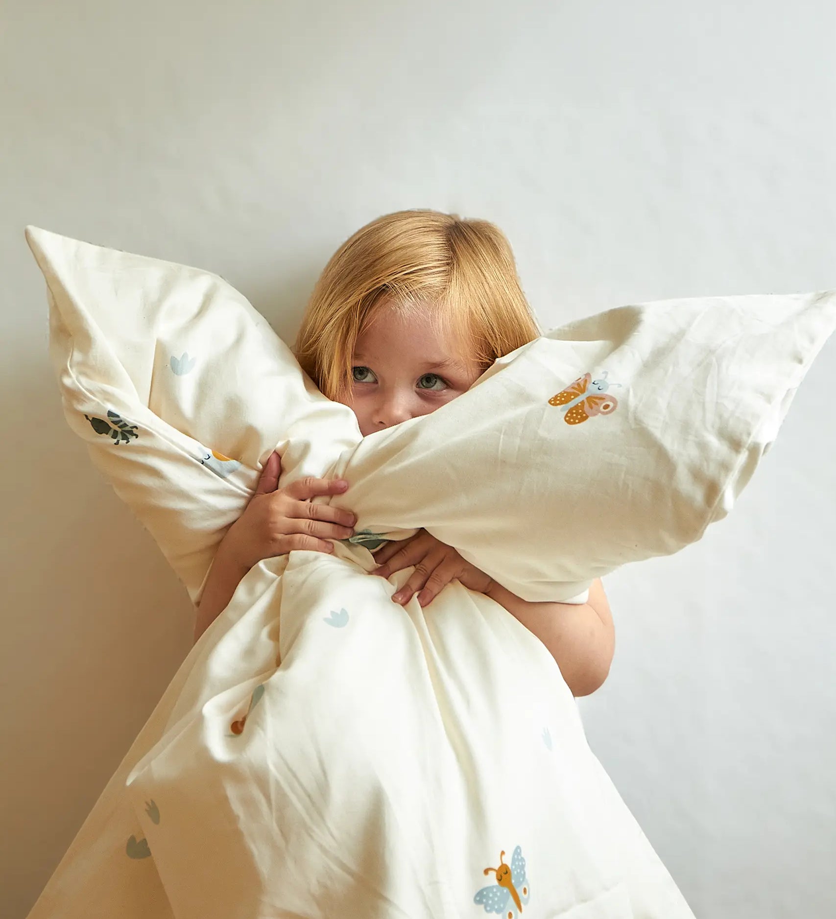 Child cuddling the Roommate single organic cotton duvet coverwith baby bugs print on a cream background. 