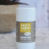 Salt Of The Earth refillable deodorant stick in natural amber and sandalwood on a marble surface with a plant in the background