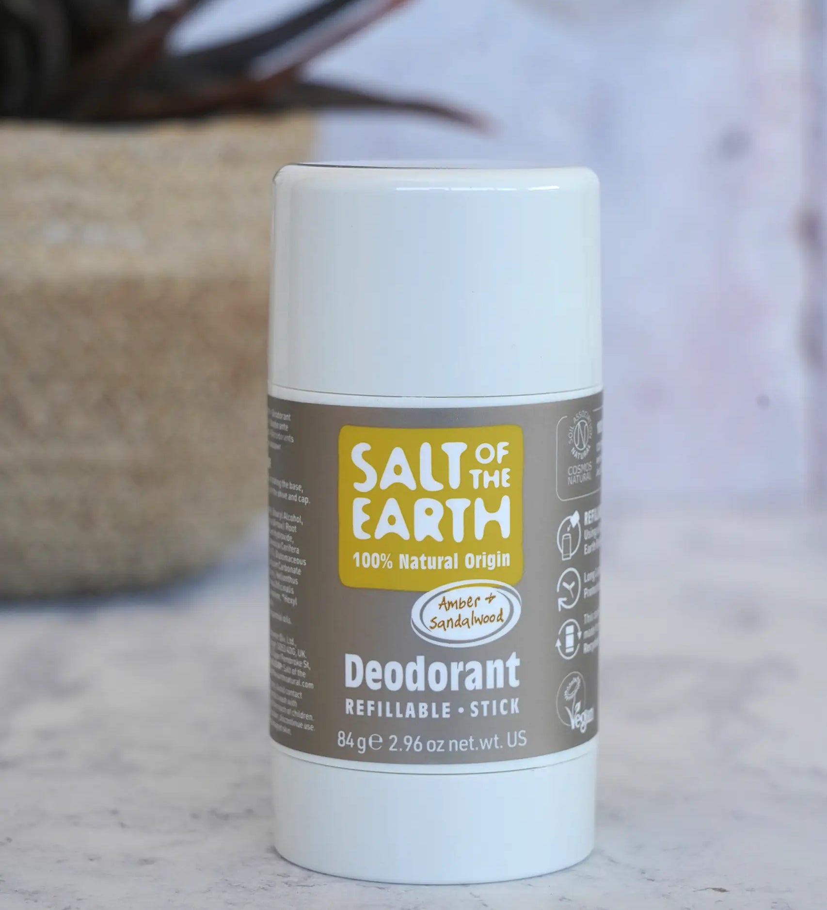 Salt Of The Earth refillable deodorant stick in natural amber and sandalwood on a marble surface with a plant in the background