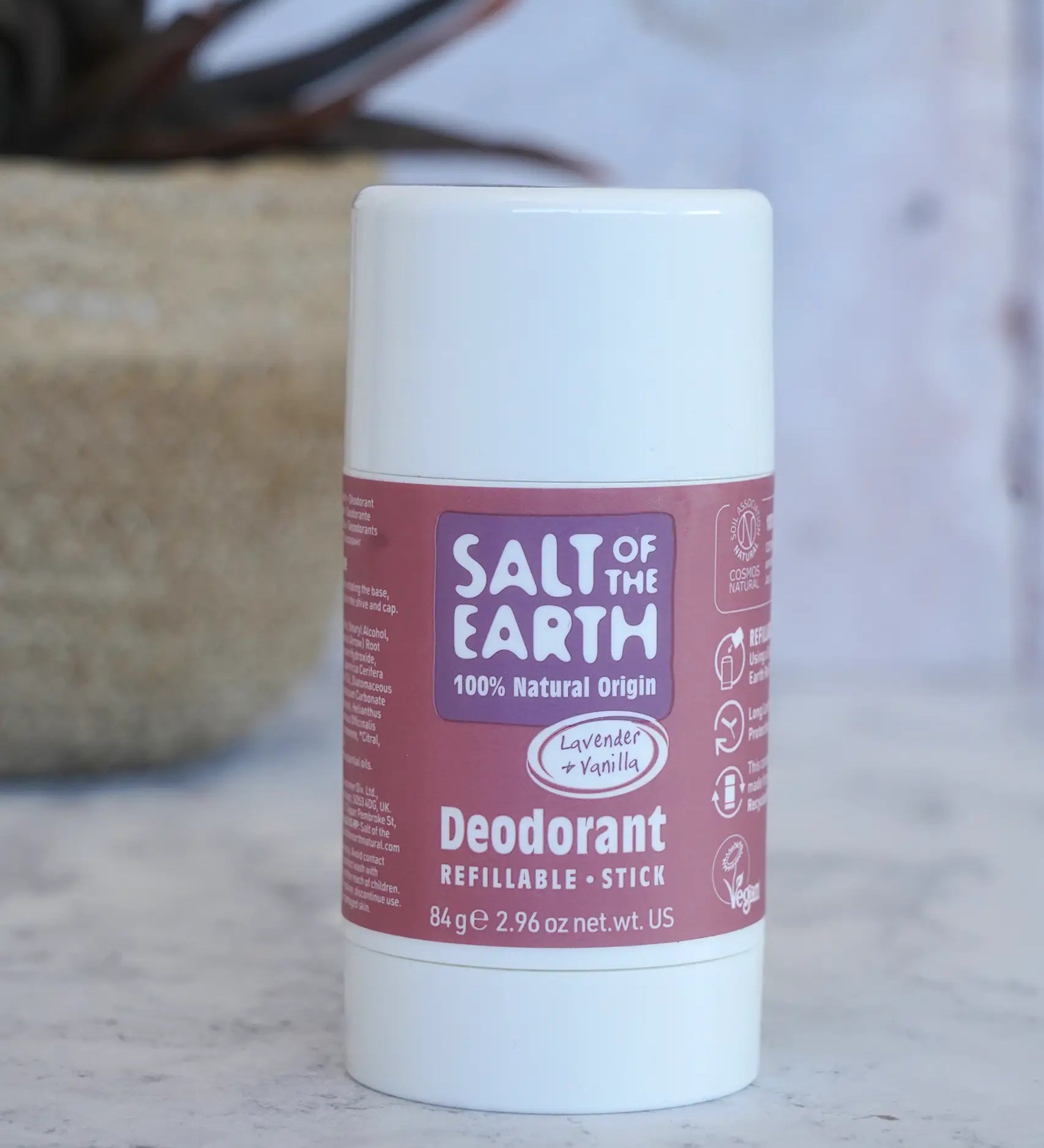 Salt Of The Earth refillable deodorant stick in natural lavender and vanilla on a marble surface with a plant in the background