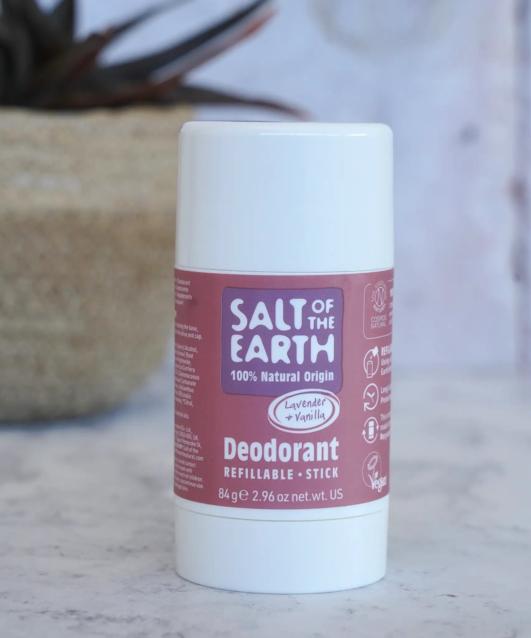Salt Of The Earth refillable deodorant stick in natural lavender and vanilla on a marble surface with a plant in the background