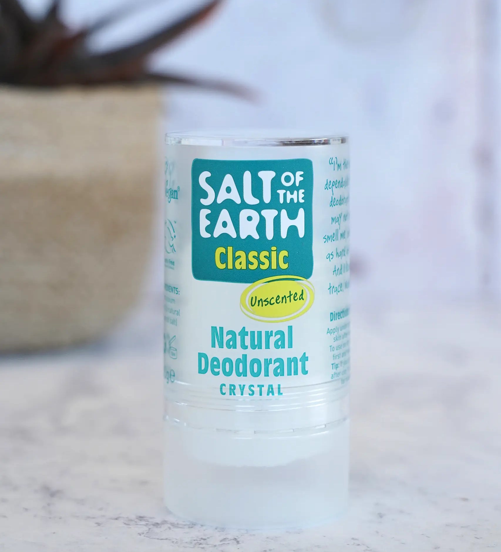 Salt Of The Earth classic unscented natural crystal deodorant stick standing on a marble surface with a plant in the background