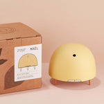 Maël Diffuser, a light yellow dome plug-in essential oil diffuser with wooden feet next to its cardboard box. 