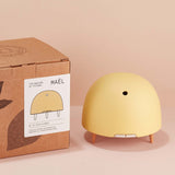 Maël Diffuser, a light yellow dome plug-in essential oil diffuser with wooden feet next to its cardboard box. 