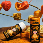 Two of The Scrubber plastic-free natural deodorant with groovy packaging standing on a metal surface under autumn coloured leaves