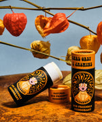 Two of The Scrubber plastic-free natural deodorant with groovy packaging standing on a metal surface under autumn coloured leaves