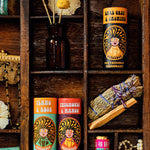 3 of The Scrubber plastic-free natural deodorant in ylang & rose, patchouli & mango and earl grey & jasmine scent with groovy packaging laid next to miscellaneous objects in a wooden display tray. 
