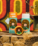 Two of The Scrubber plastic-free natural deodorant in ylang & rose with groovy packaging standing on a wooden surface with a psychedelic backdrop. 