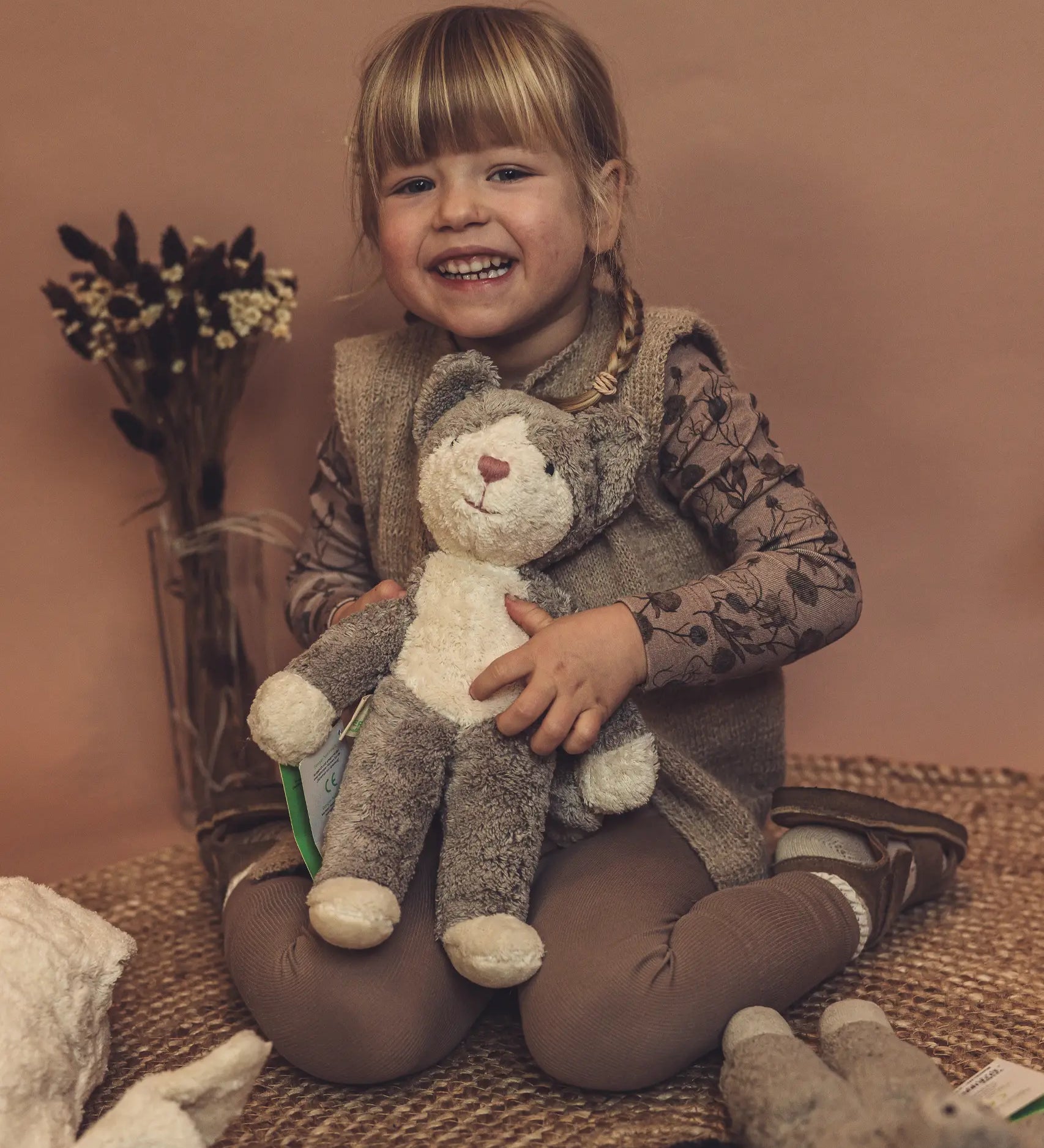 Child holding a GOTS organic cotton Senger baby grey and white cat soft toy. 