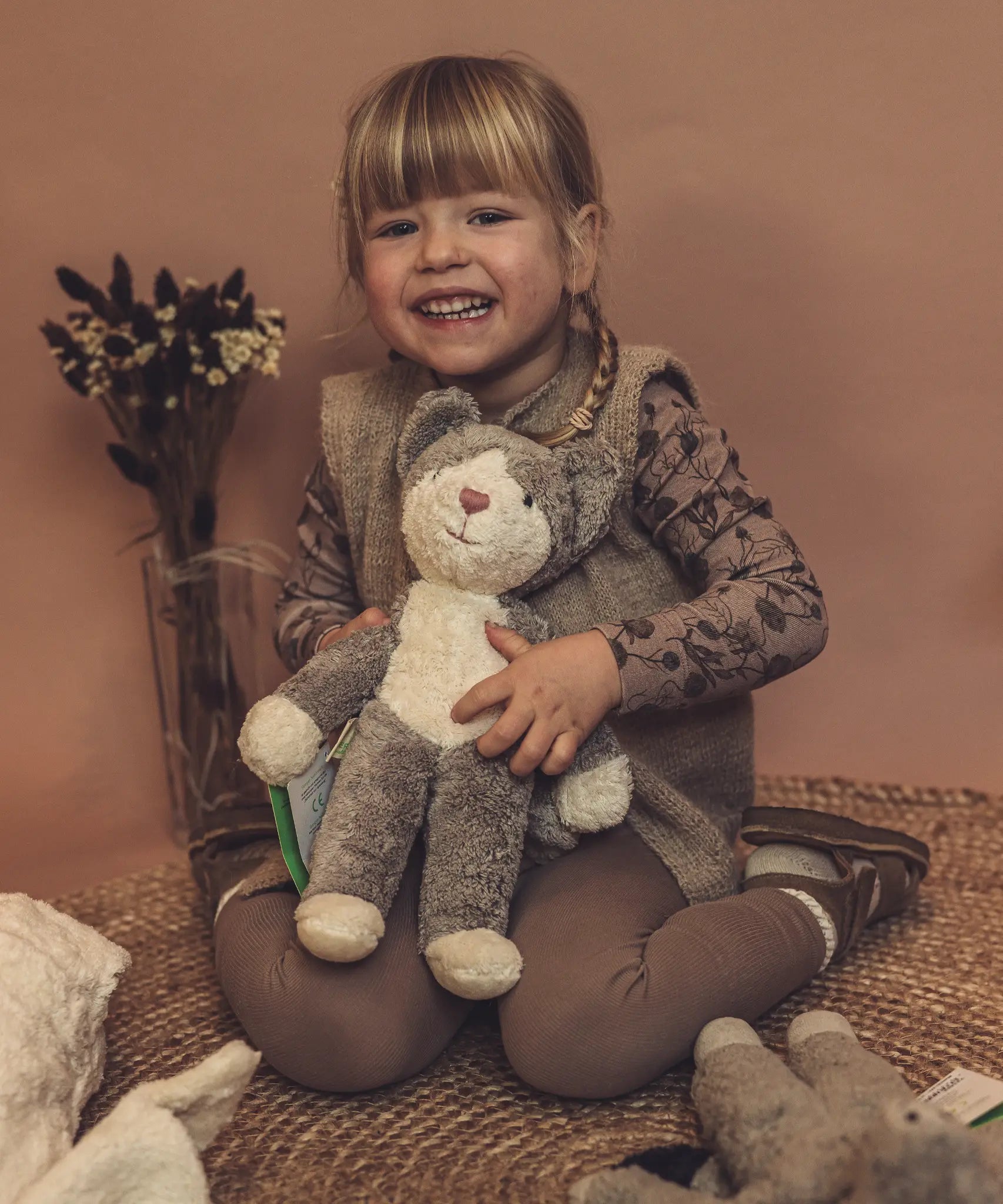 Child holding a GOTS organic cotton Senger baby grey and white cat soft toy. 