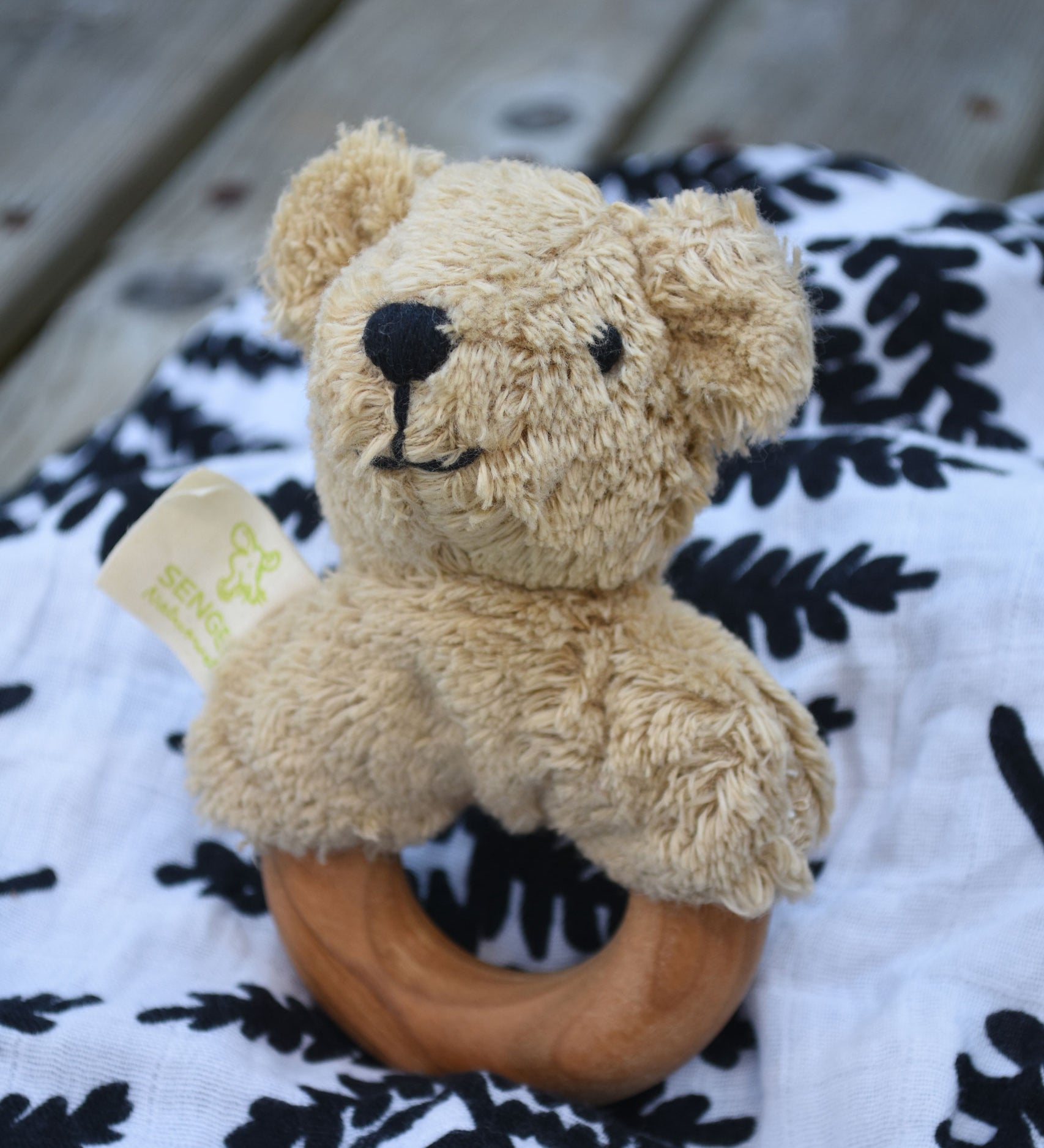 A Senger bear baby grasping toy placed on an Etta Loves fern print sensory muslin cloth.