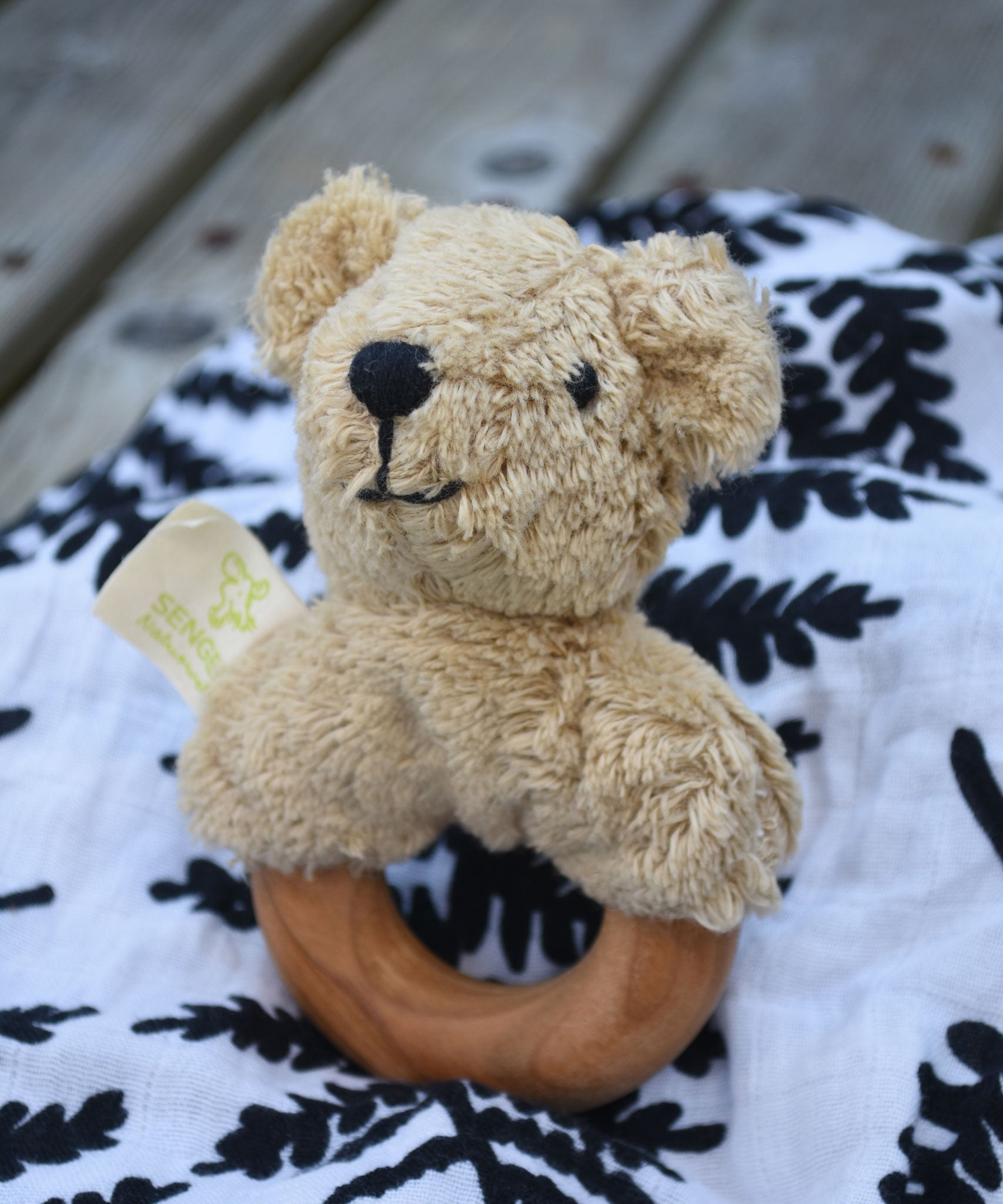 A Senger bear baby grasping toy placed on an Etta Loves fern print sensory muslin cloth.