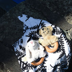 Senger bear and sheep baby grasping toys placed on an Etta Loves fern print sensory muslin cloth on a stone wall outdoors.