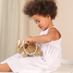 A child sitting down with a Senger beige Rabbit Bag on their lap. they are opening the zip of the bag. 