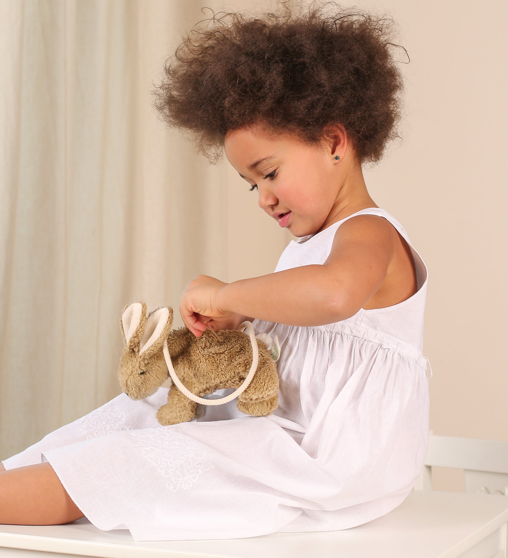 A child sitting down with a Senger beige Rabbit Bag on their lap. they are opening the zip of the bag. 