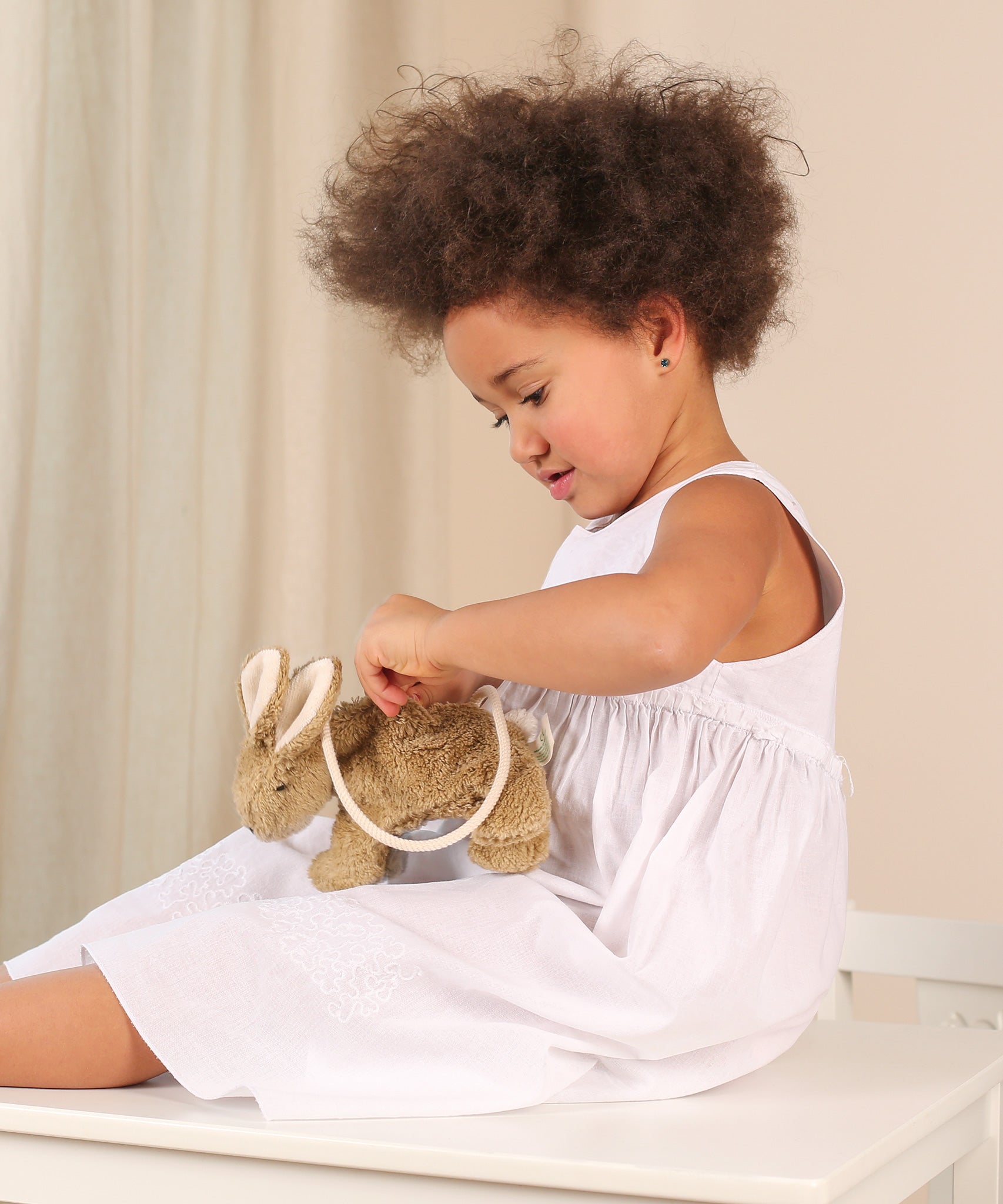 A child sitting down with a Senger beige Rabbit Bag on their lap. they are opening the zip of the bag. 