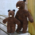 A Senger baby beaver propped up next to a small floppy baby beaver on wooden decking. 
