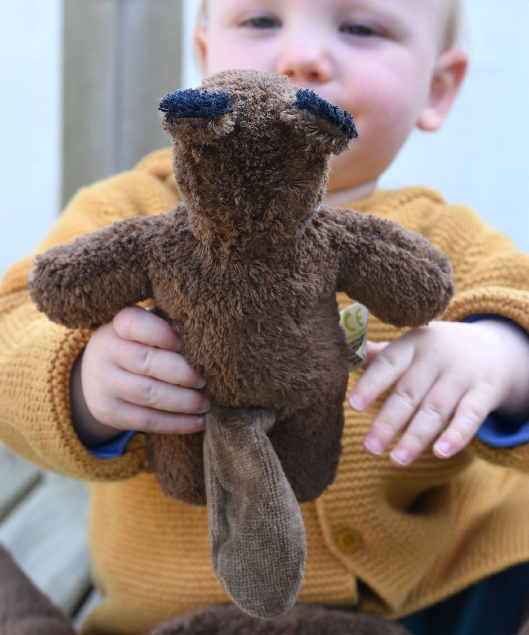 A close up of a Senger Baby Beaver Organic Soft Toy in a child's hands, the beaver is facing away from the camera and the tail can be seen.