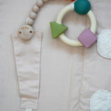 A natural rubber Hevea pacifier holder clip attached to the Senger Cozy Nap Playmat, with an Oli & Carol rubber teether attached.
