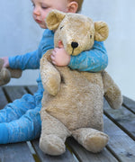 A young child holding the large Senger beige bear in the crook of their arm.