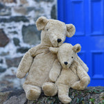 A large and small Senger cuddly beige bear sat next to each other on a stone wall.
