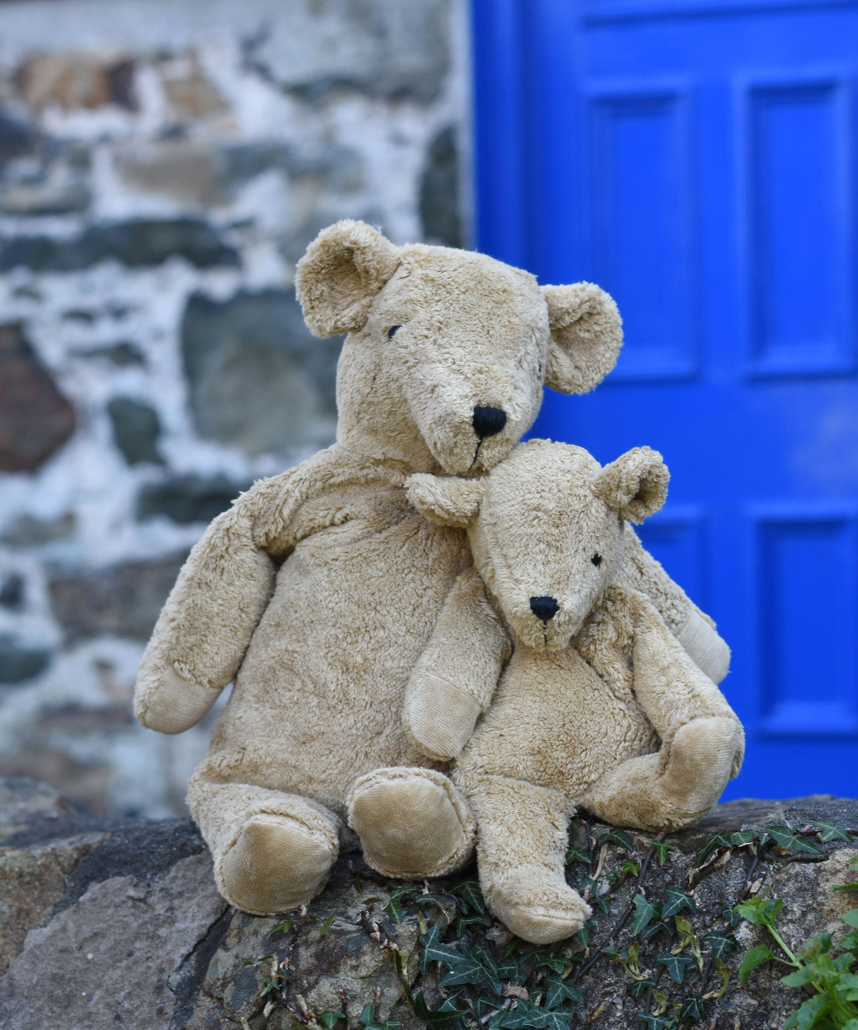 A large and small Senger cuddly beige bear sat next to each other on a stone wall.