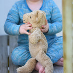 A close up of a small Senger beige cuddly teddy bear in a child's hands. The side of the teddy is facing the camera.