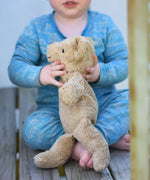 A close up of a small Senger beige cuddly teddy bear in a child's hands. The side of the teddy is facing the camera.