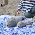 A large and small cuddly Senger grey seal placed on a blue and white patterned blanket on the back. A child can be seen in the background.  
