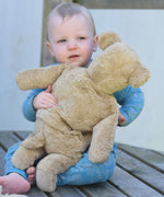 A young child holding the large Senger beige bear, the teddy is facing the child and it's back is facing the camera.