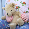 A close up of a small Senger beige cuddly teddy bear in a child's hands.