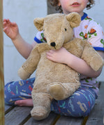 A close up of the large organic cotton Senger cuddly beige bear held in a child's arm.