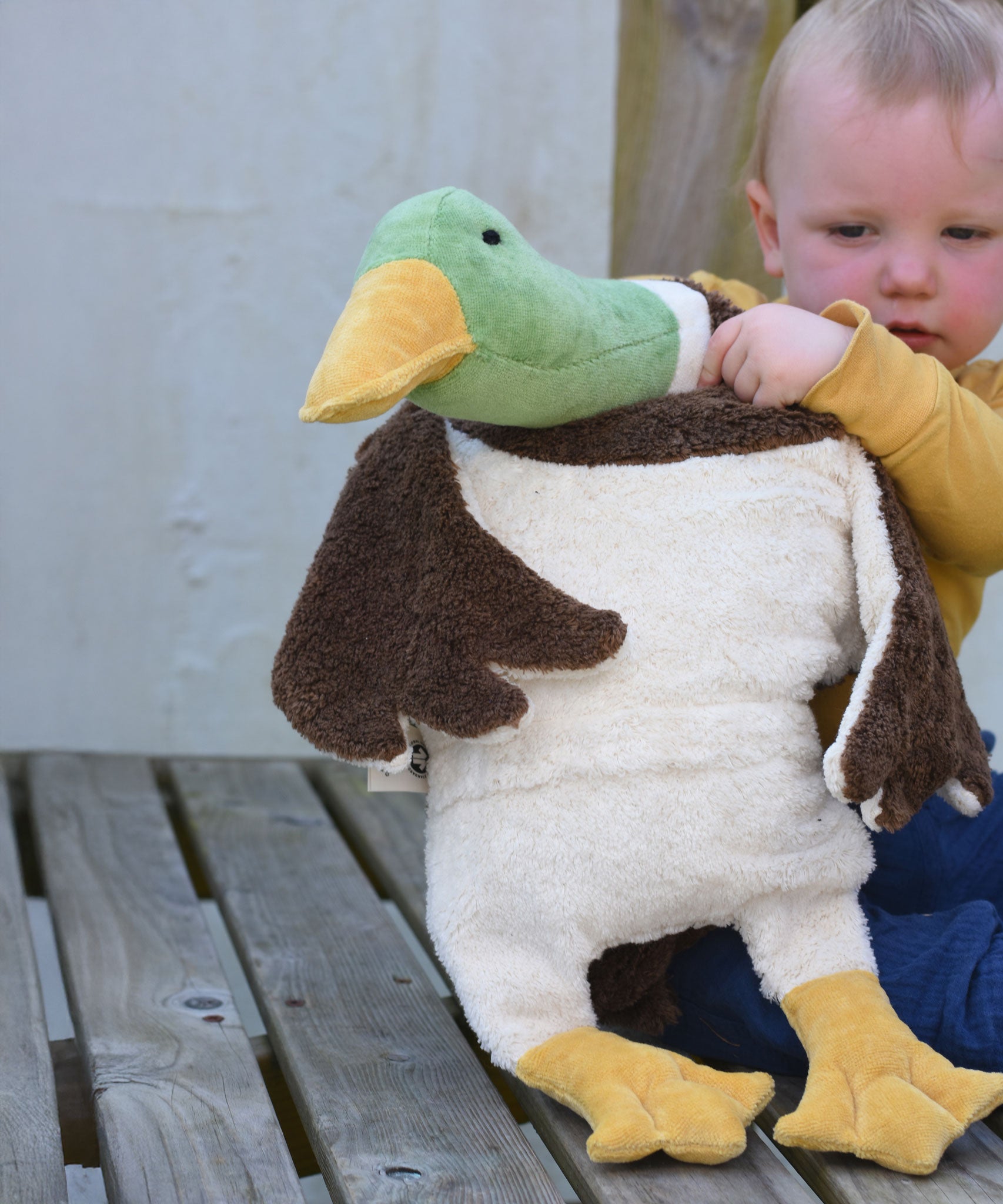 A child holding up a Senger Large Cuddly Drake Duck soft toy showing the white underside of the duck. 