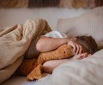 A child laying in bed cuddling a Senger Small Cuddly Goose organic soft toy in a dark orange Rust colour. These soft toys are created from the highest quality, sustainable and traceable natural materials. Senger cuddly animal toys and soft dolls are handmade in Germany with love and attention to detail and we are proud Senger stockists here at Babipur. 