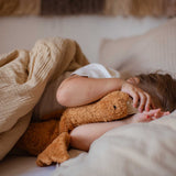 A child laying in bed cuddling a Senger Small Cuddly Goose organic soft toy in a dark orange Rust colour. These soft toys are created from the highest quality, sustainable and traceable natural materials. Senger cuddly animal toys and soft dolls are handmade in Germany with love and attention to detail and we are proud Senger stockists here at Babipur. 