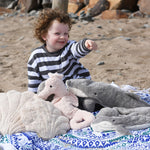 A child sitting on a blue and white patterned blanket with a  collection of sea life themed cuddly animals from Senger placed in front of them.